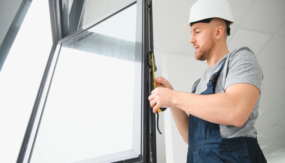 Workman in overalls installing or adjusting plastic windows in the living room at home